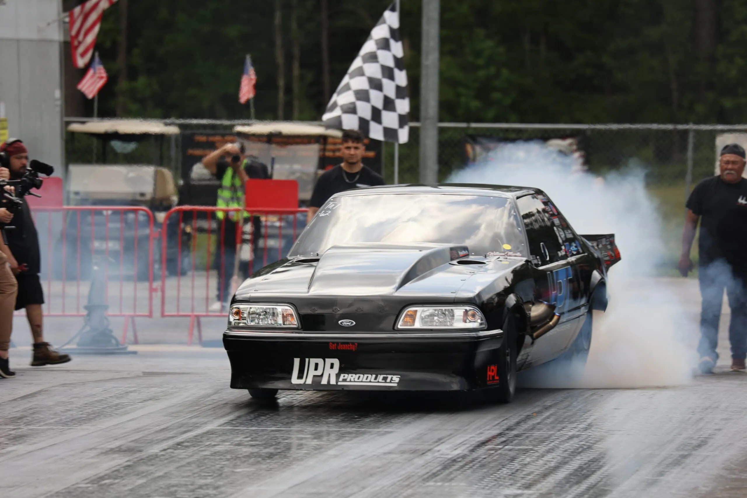 Black drag racing Mustang performing burnout at Mustang Week event.