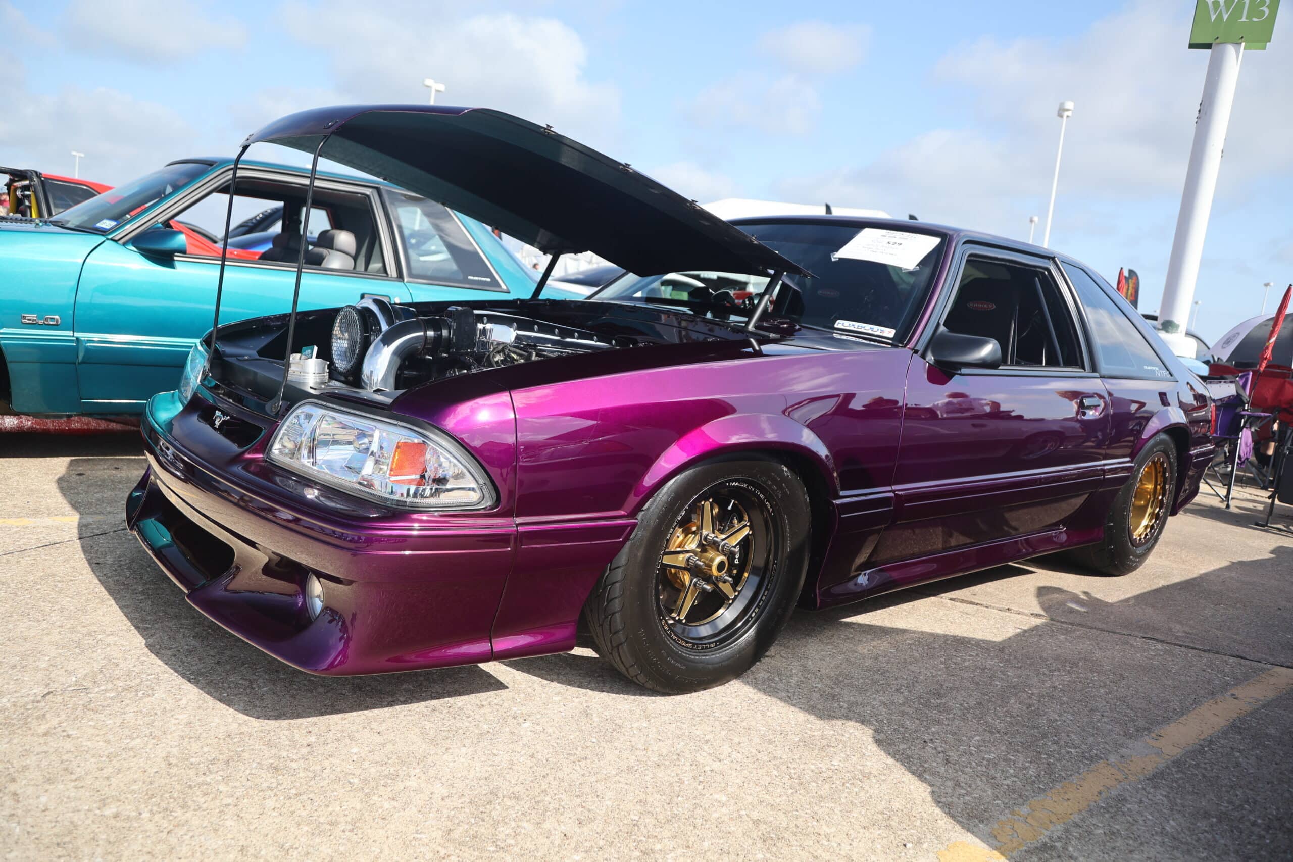 Purple modified Mustang with open hood at Mustang Week event.