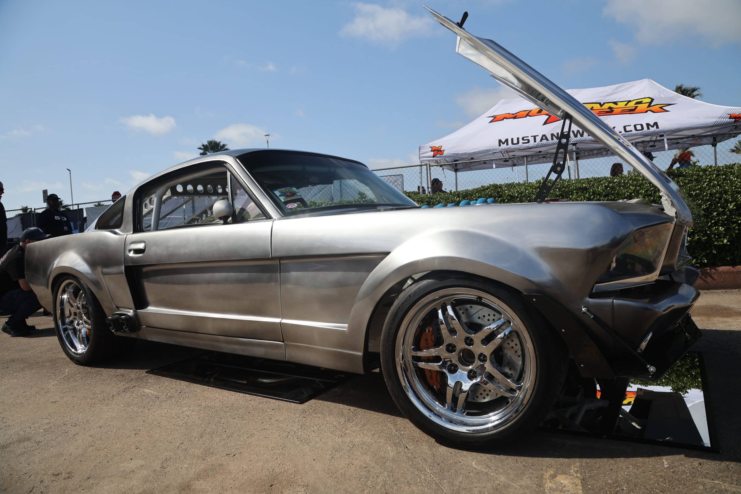 Sleek silver Mustang with open hood at Mustang Week event.