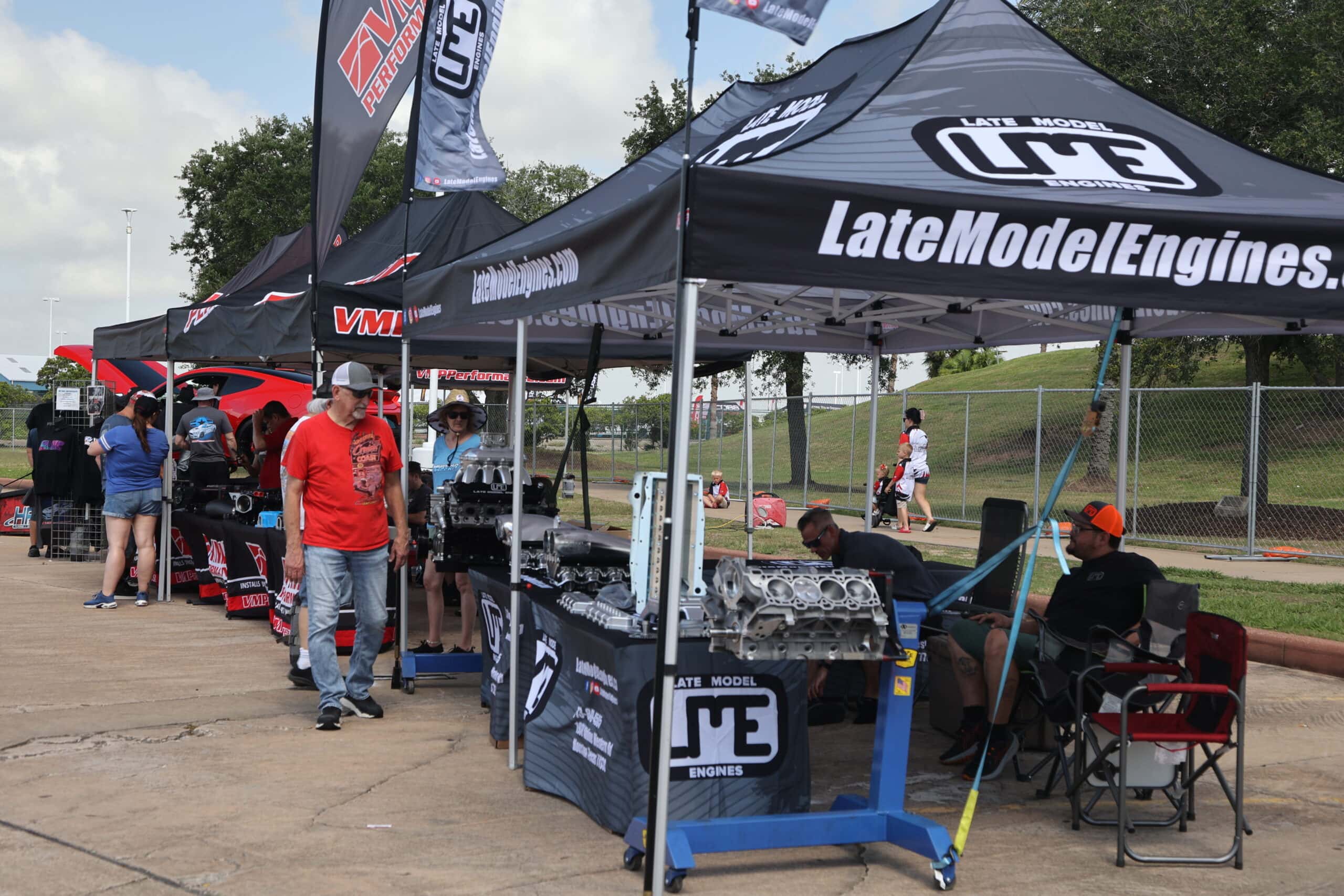 Car enthusiasts at Mustang Week with engine displays and vendor tents in Texas 2025.