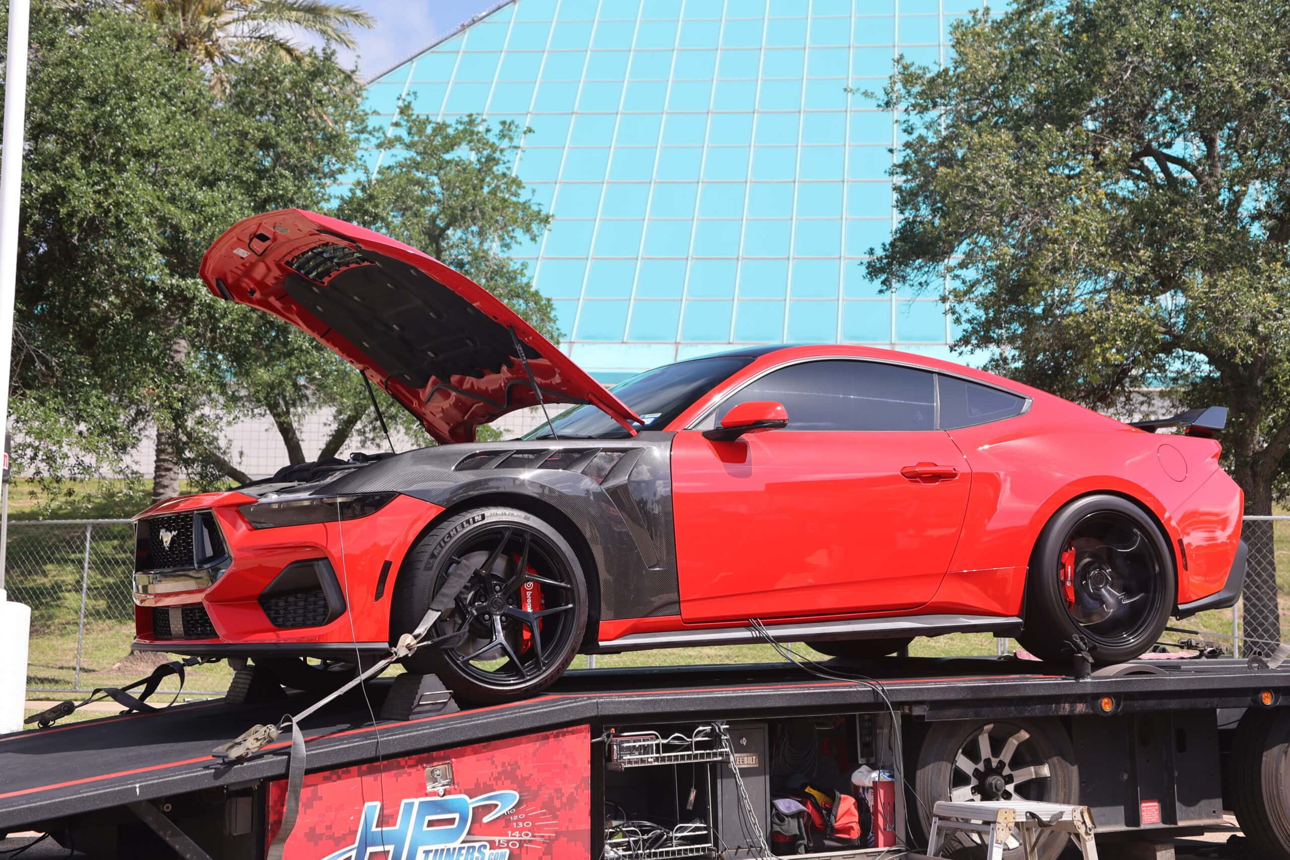 Red and black Ford Mustang on a trailer at Mustang Week event.