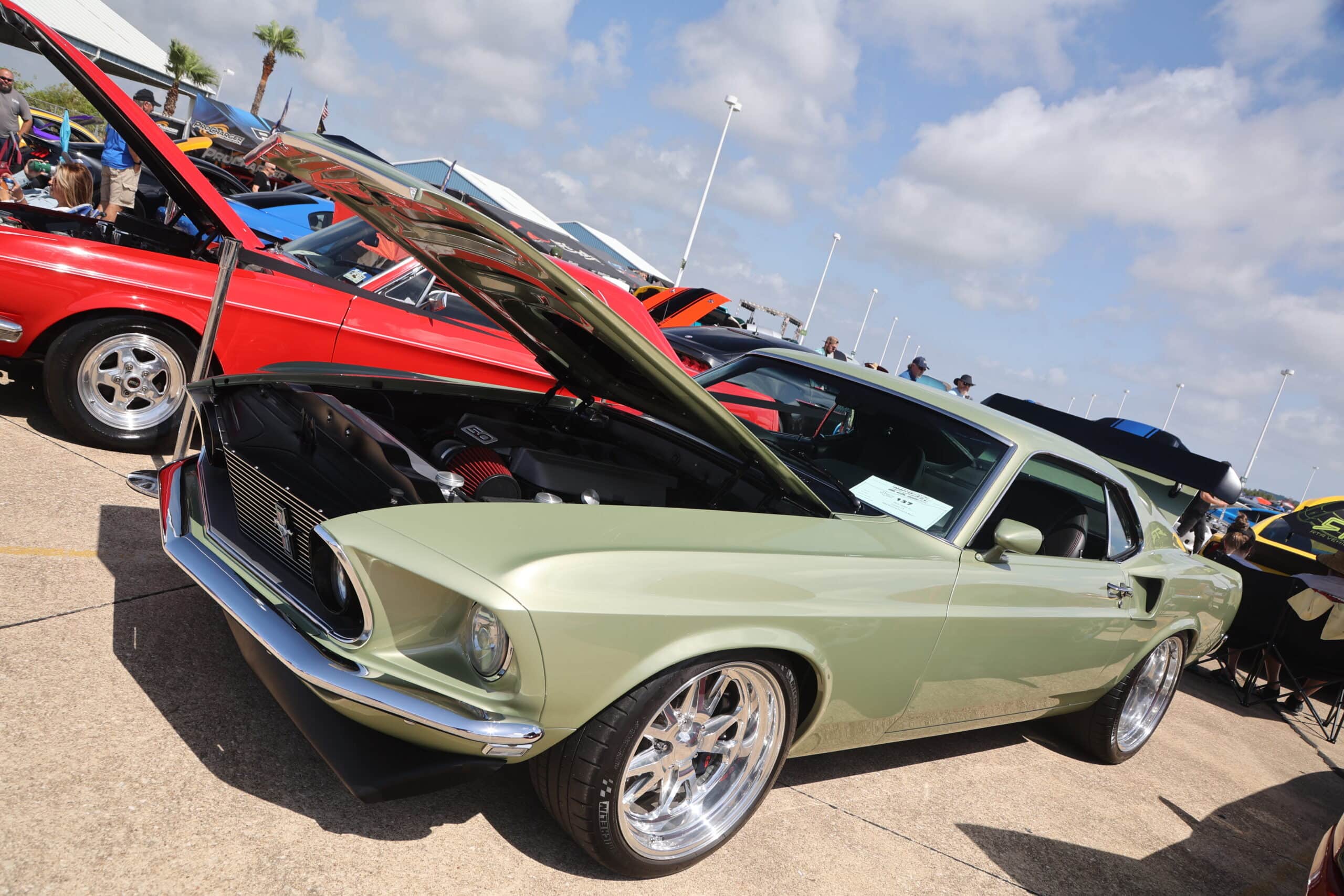 Green vintage Ford Mustang with open hood at Mustang Week event.