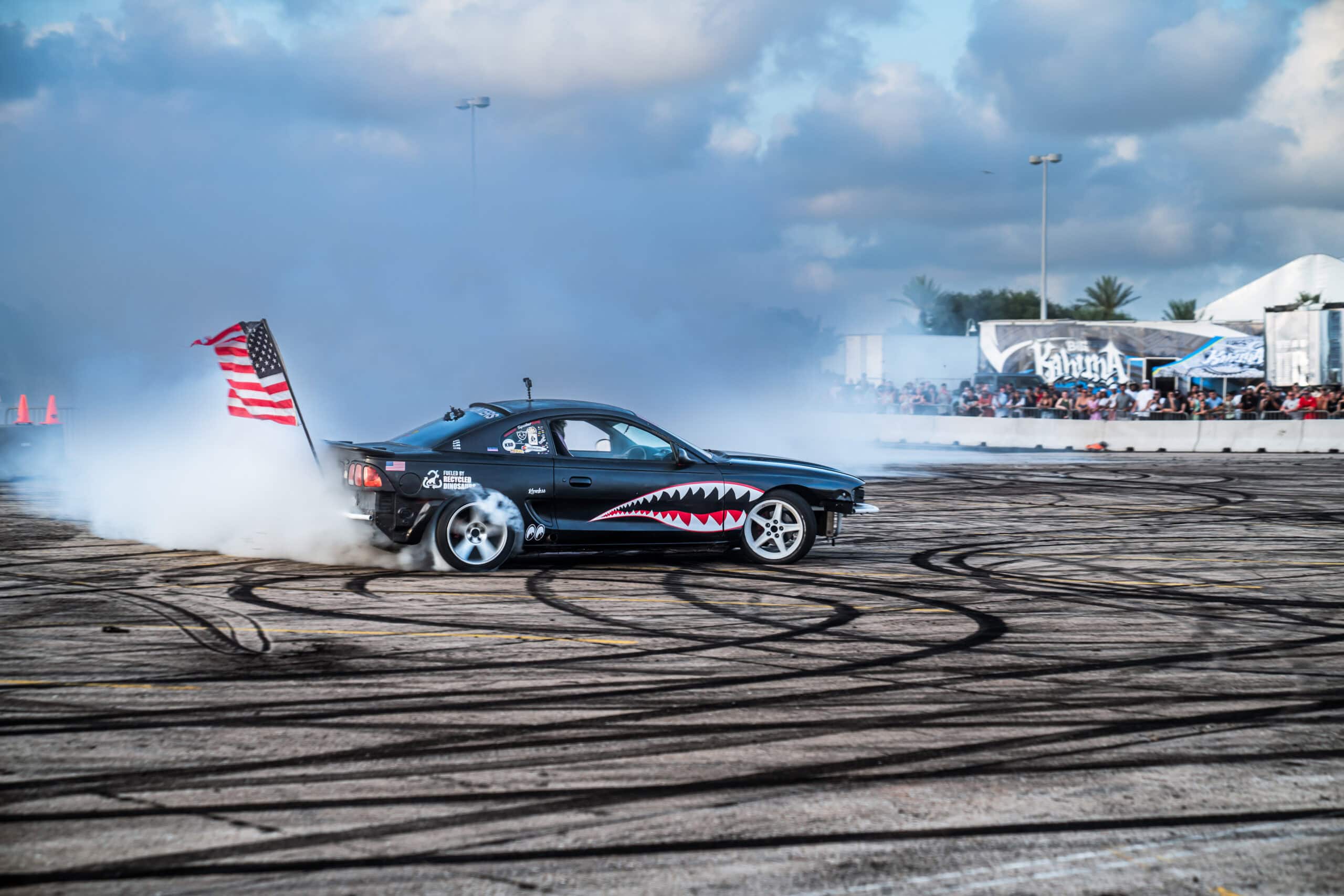 Black Mustang with American flag drifting at Mustang Week event.