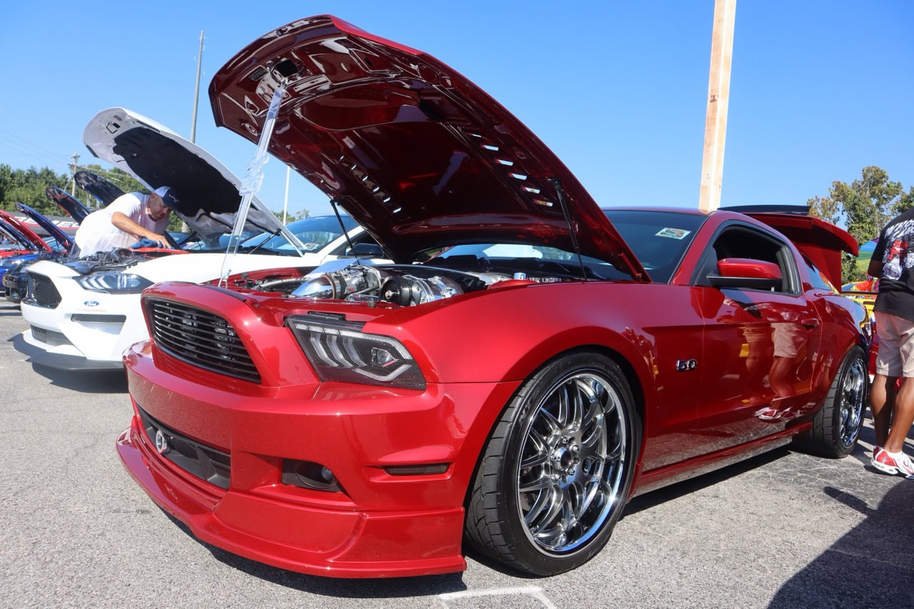 Mustang Week car show featuring a red Ford Mustang with custom wheels and open hood.