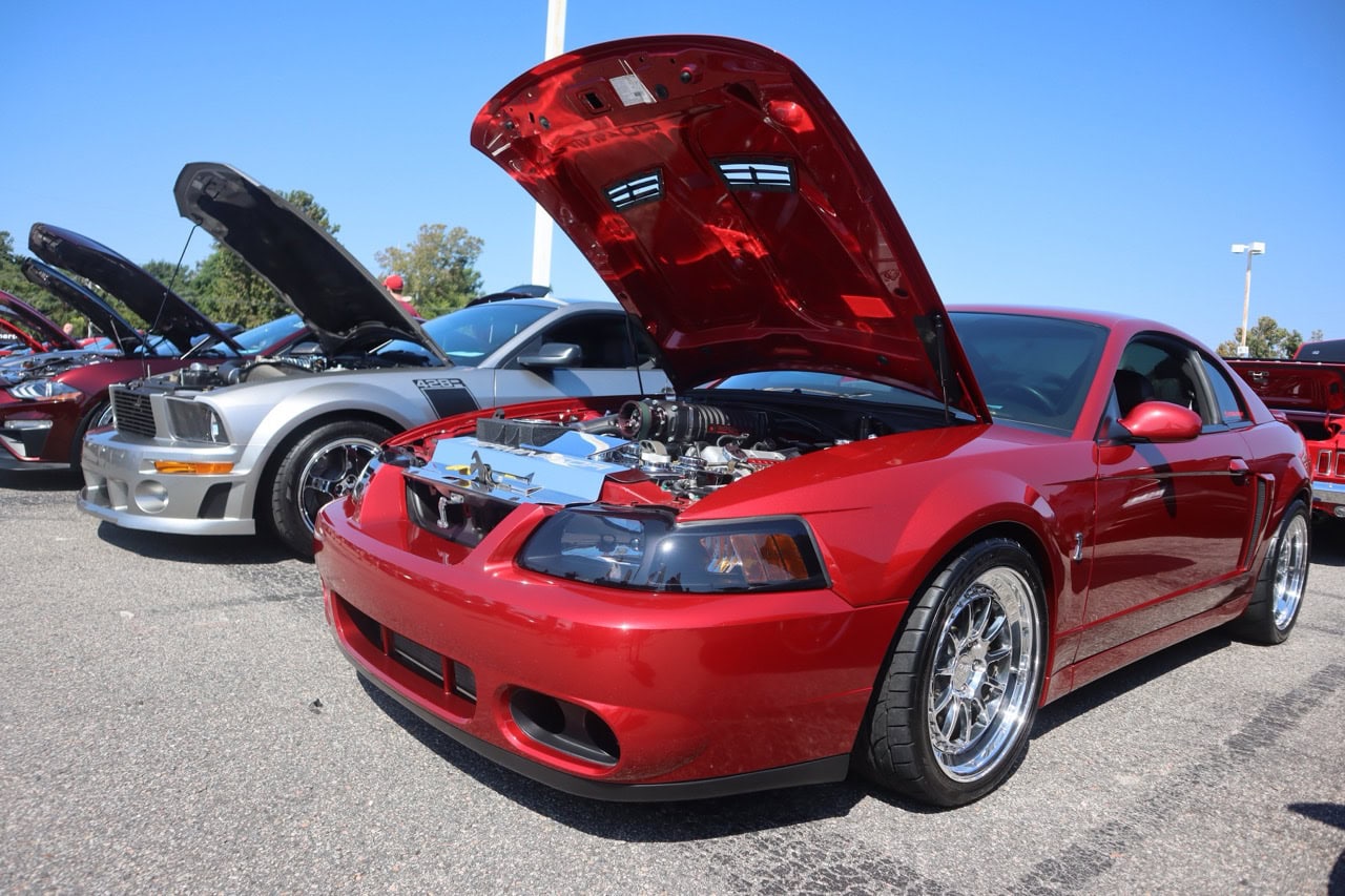 Red Ford Mustang with open hood at car show.