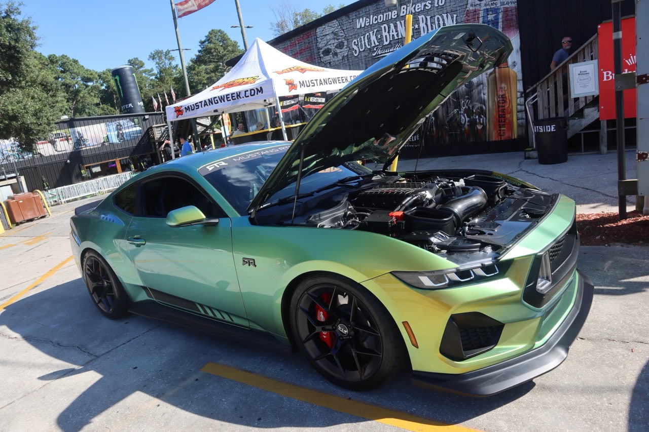 High-performance green Ford Mustang with open hood at Mustang Week event.
