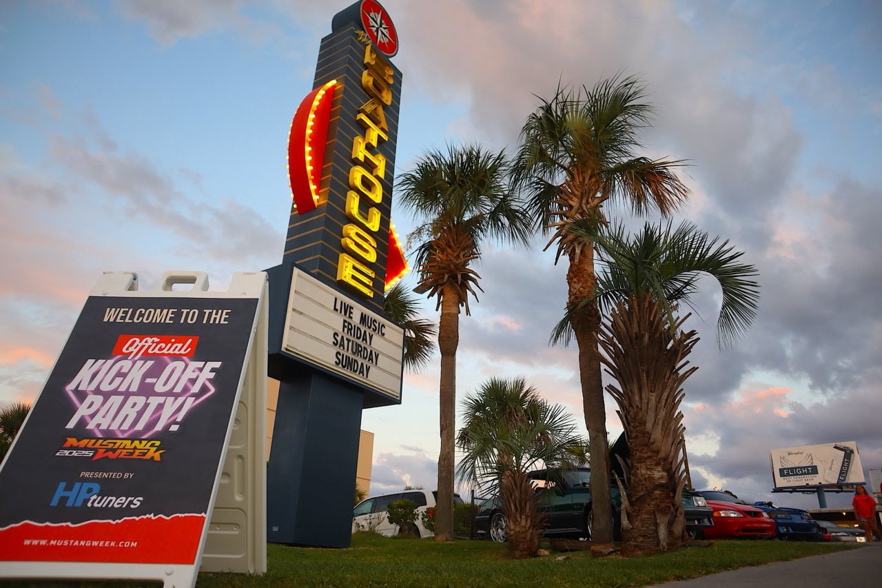 Mustang Week sign at Myrtle Beach with palm trees and event banners.