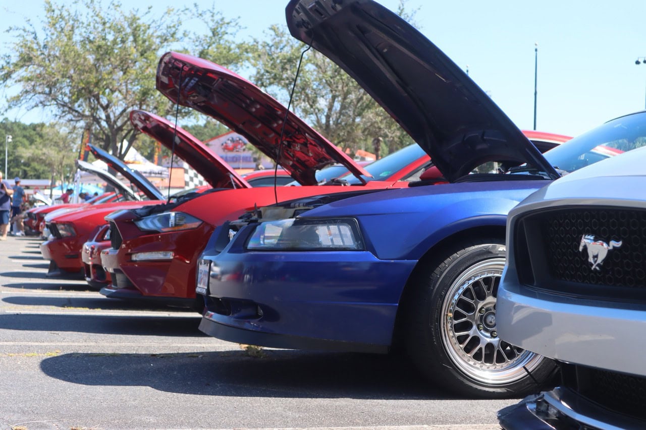 Lineup of colorful Ford Mustangs at Myrtle Beach car event with open hoods.