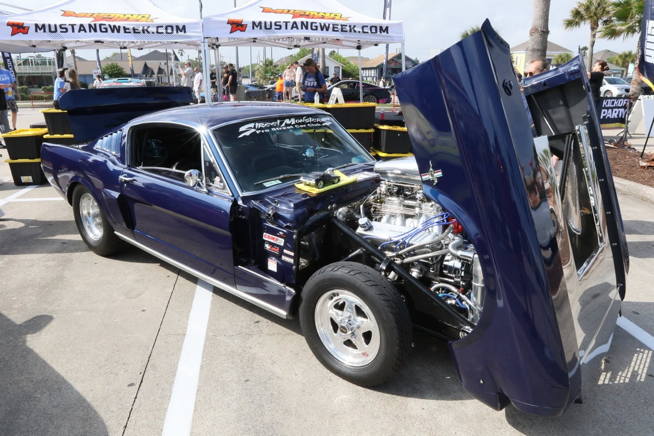 Classic blue muscle car with open hood at Mustang Week event.