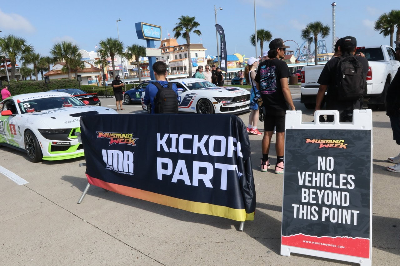 Mustang Week kickoff event with race cars and attendees at the beachside parking lot.