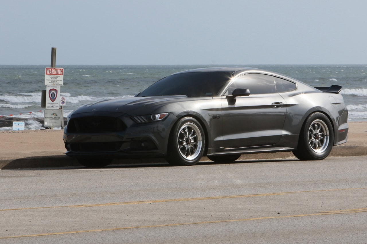 Black Ford Mustang parked by the ocean during Mustang Week event.