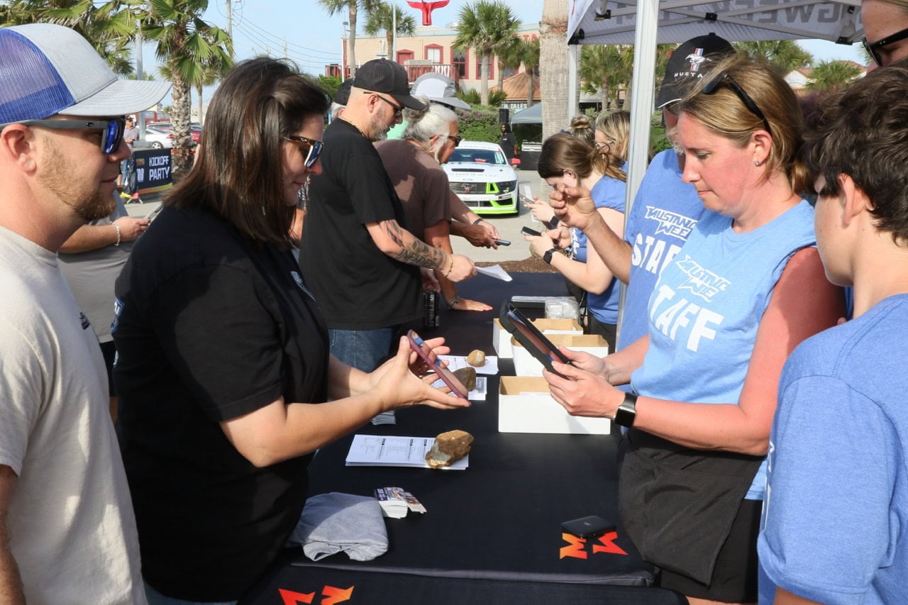 People registering for Mustang Week car event at outdoor booth.