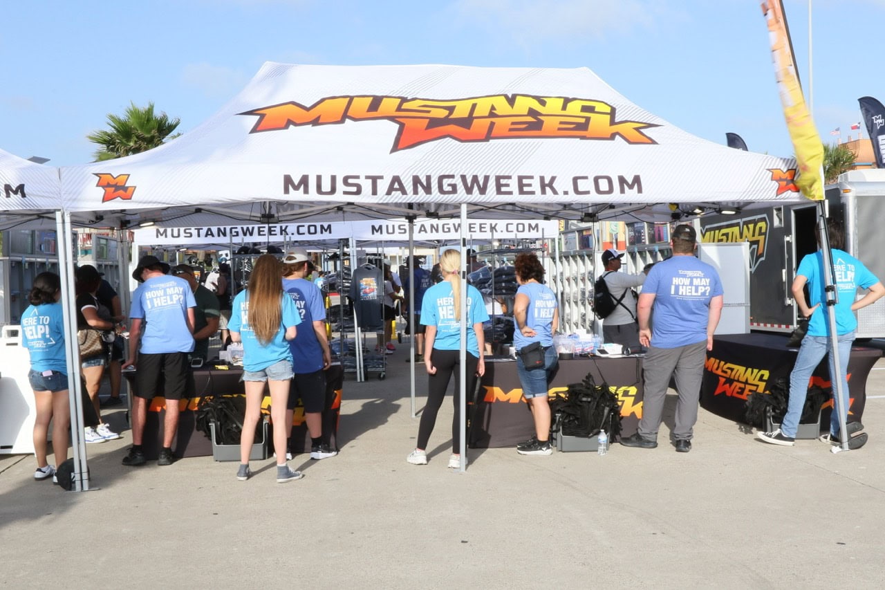 Mustang Week event tent with attendees and staff in blue shirts.