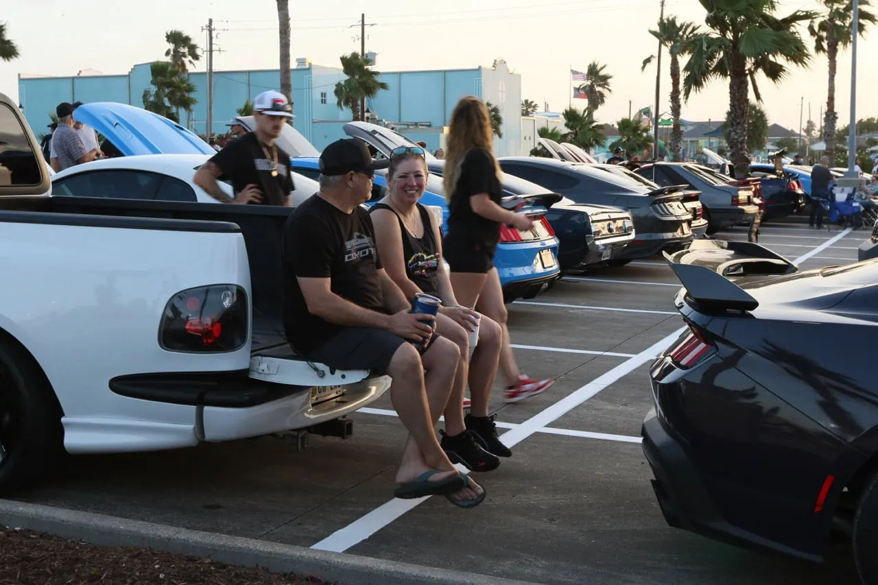 People enjoying Mustang Week car gathering in a parking lot.