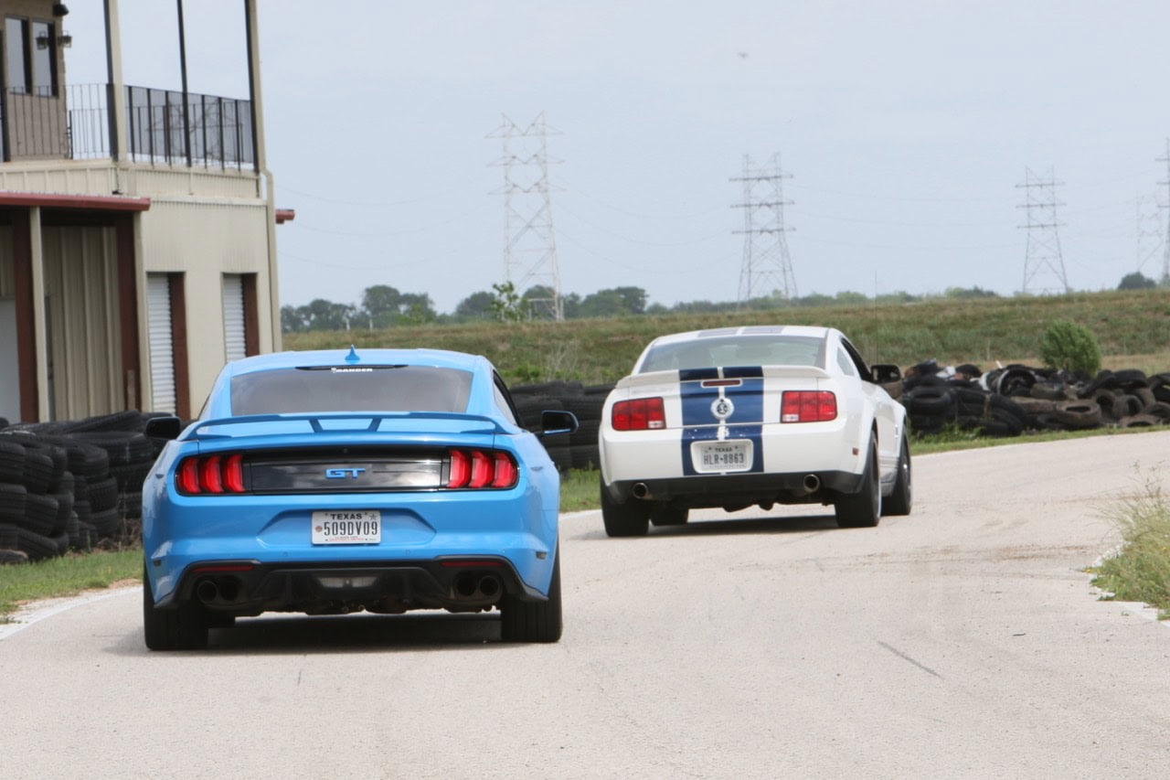 Mustang Week car meet in Texas 2026, featuring a blue Ford Mustang and a white vehicle on a race tra.