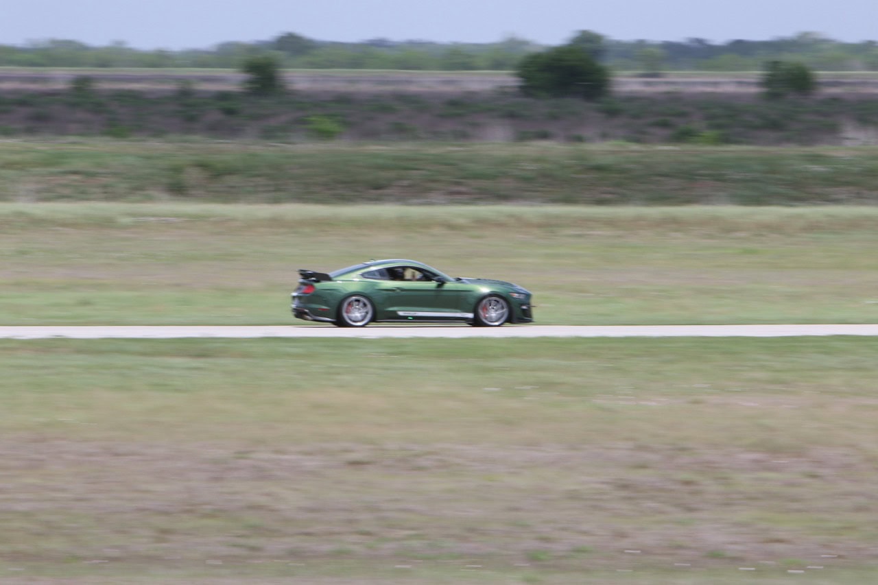 Green Ford Mustang driving on open road during Mustang Week event.