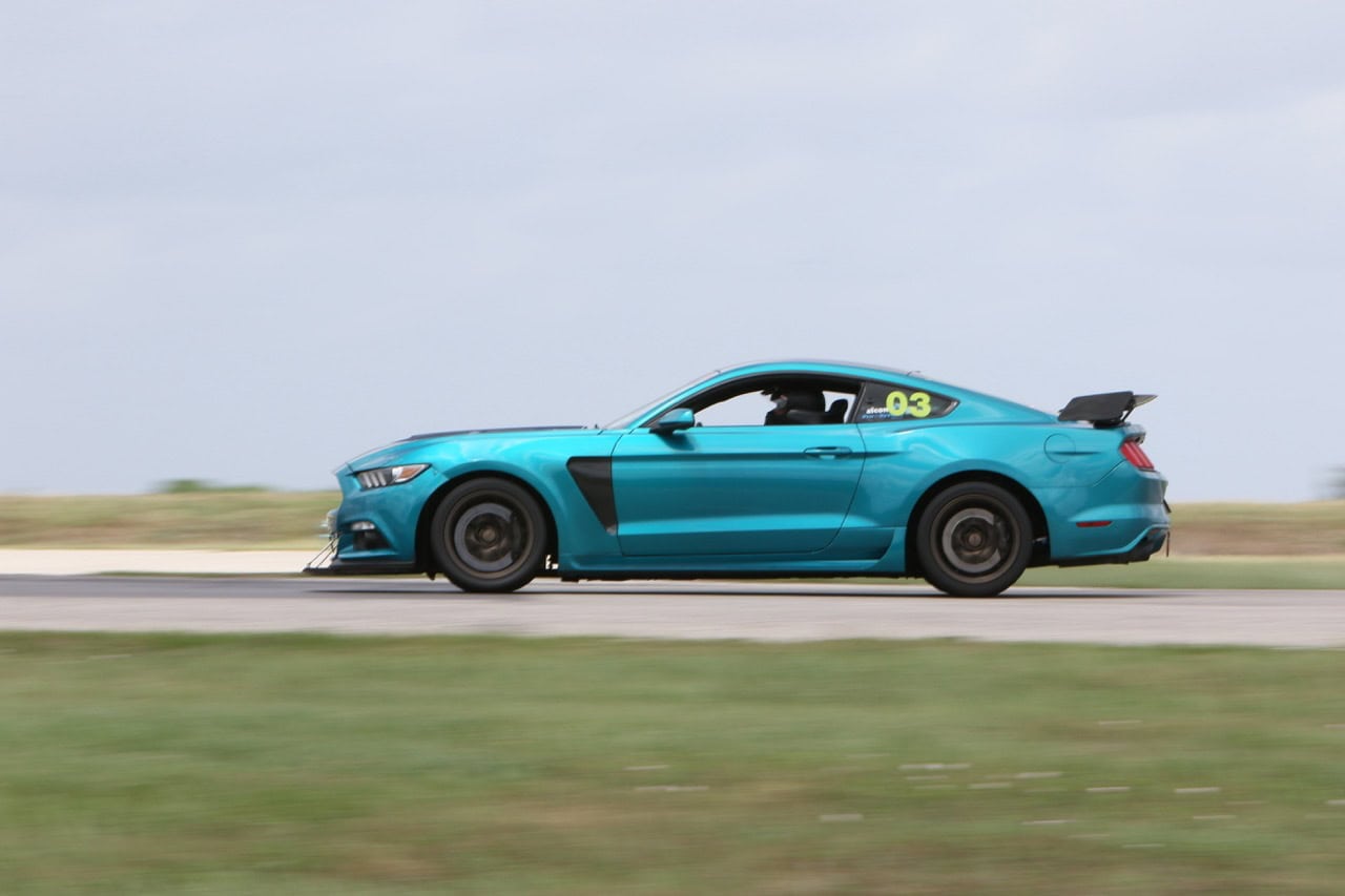High-speed blue Mustang racing on track during Mustang Week event.