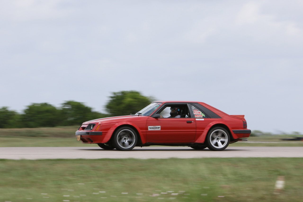 Classic red Ford Mustang racing on open road during Mustang Week event.