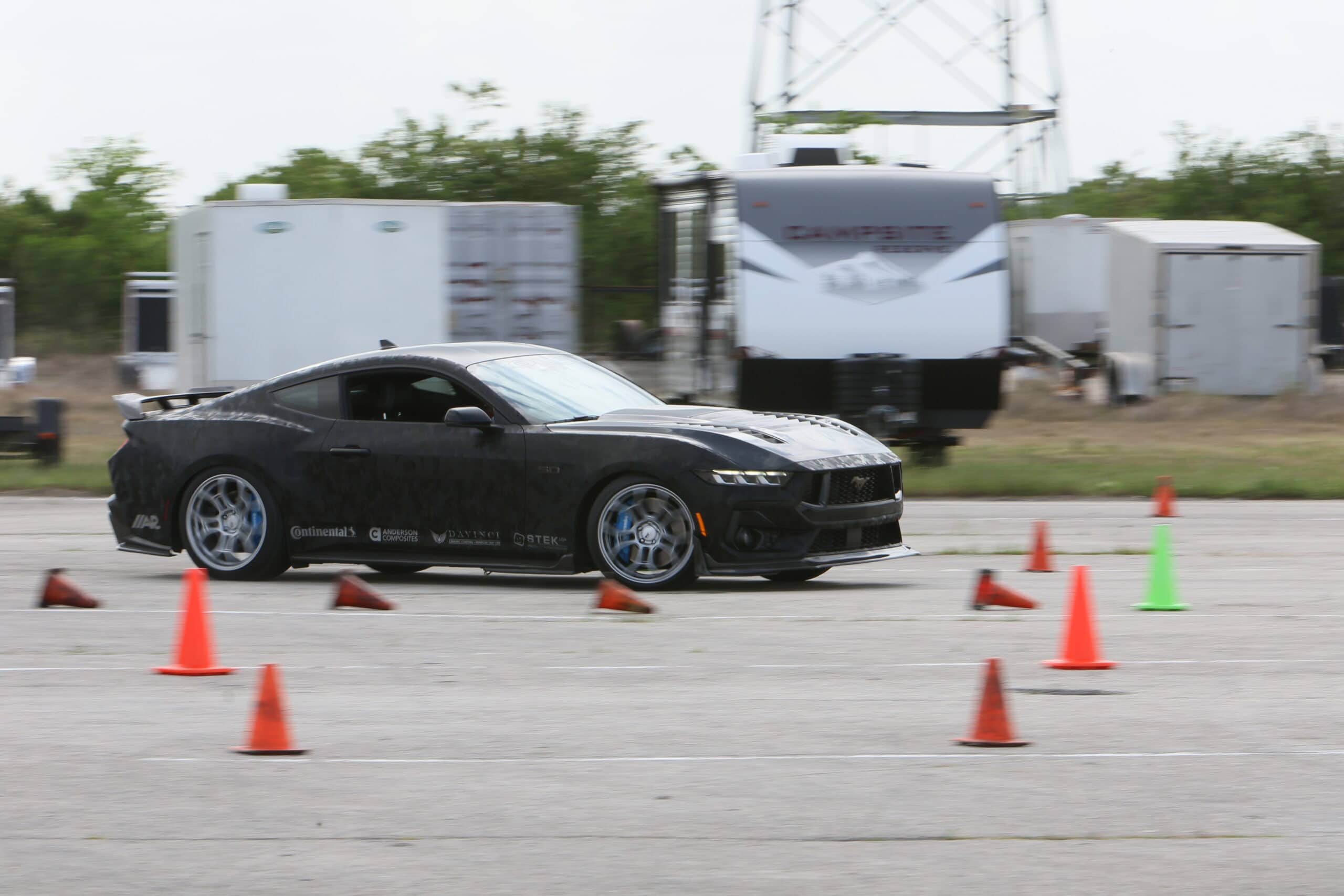 Mustang Week car event with a black Ford Mustang navigating a slalom course.