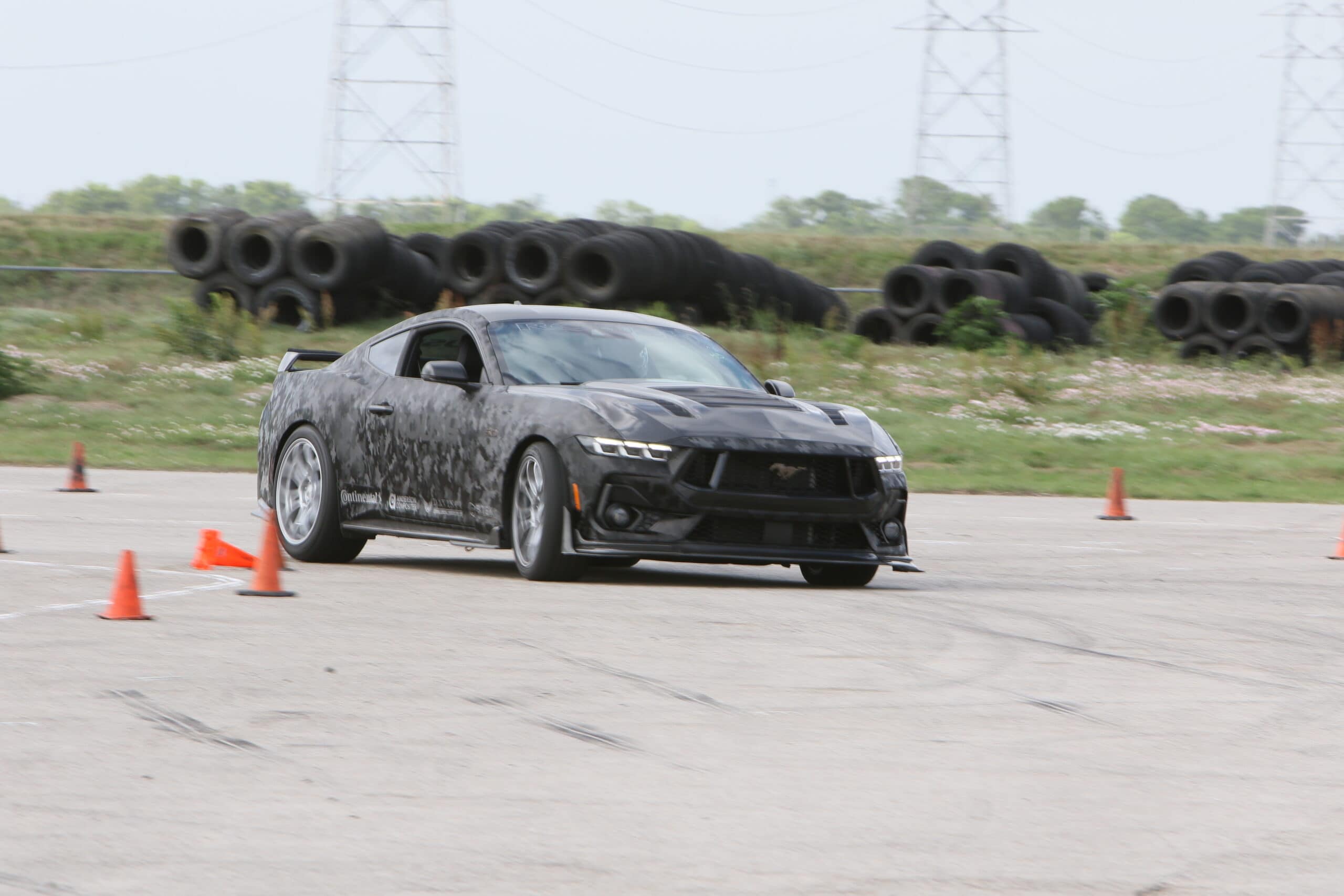Black Ford Mustang drifting during Mustang Week event on an open track.