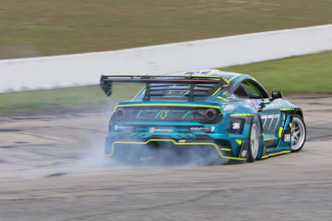 High-performance Mustang race car drifting on track during Mustang Week event.