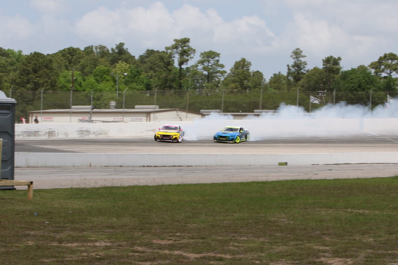 Two Ford Mustangs drifting on a race track during Mustang Week event.