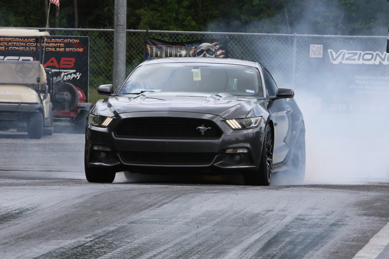 Mustang Week drag racing event with a black Ford Mustang on the track.