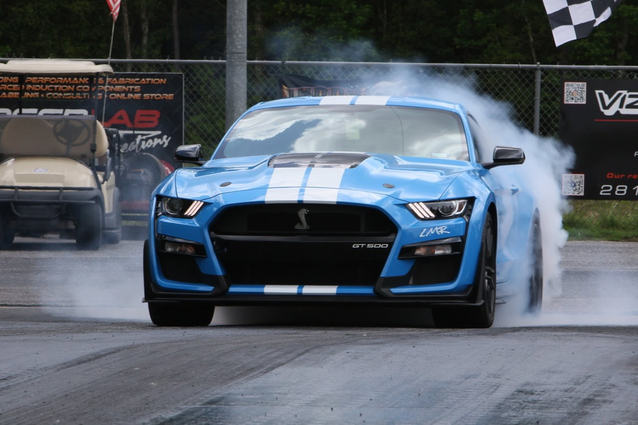 Blue Ford Mustang GT350 racing on track during Mustang Week event.