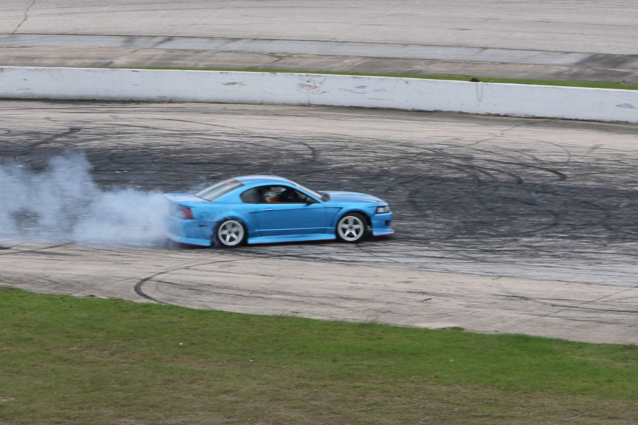 Blue Mustang drifting on race track during Mustang Week event.