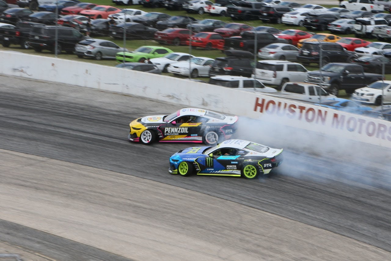 Two Ford Mustangs racing on a dirt track at Mustang Week event.