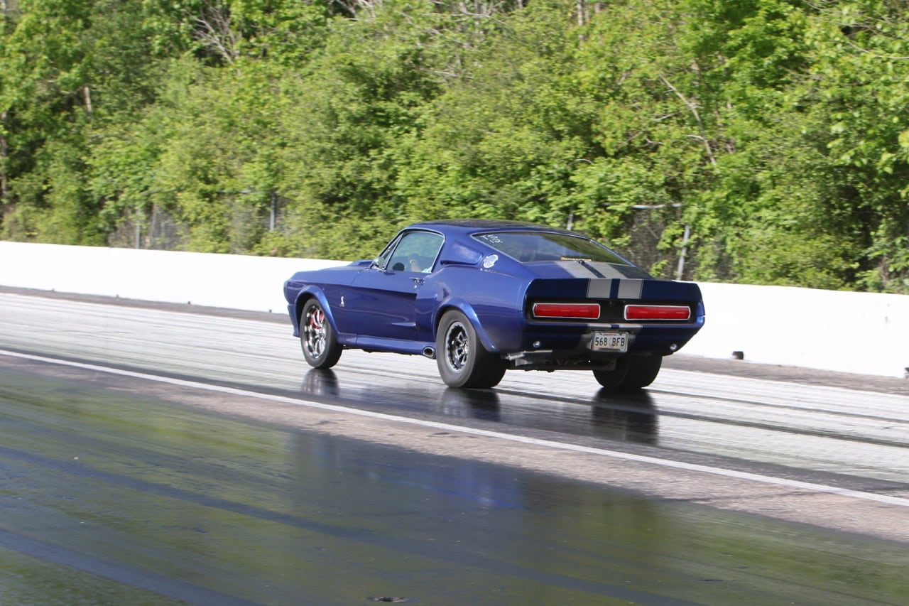 Blue vintage Ford Mustang racing on track during Mustang Week event.