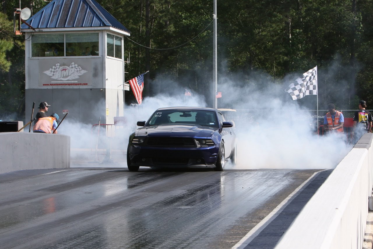 Black muscle car performing burnout at Mustang Week event.
