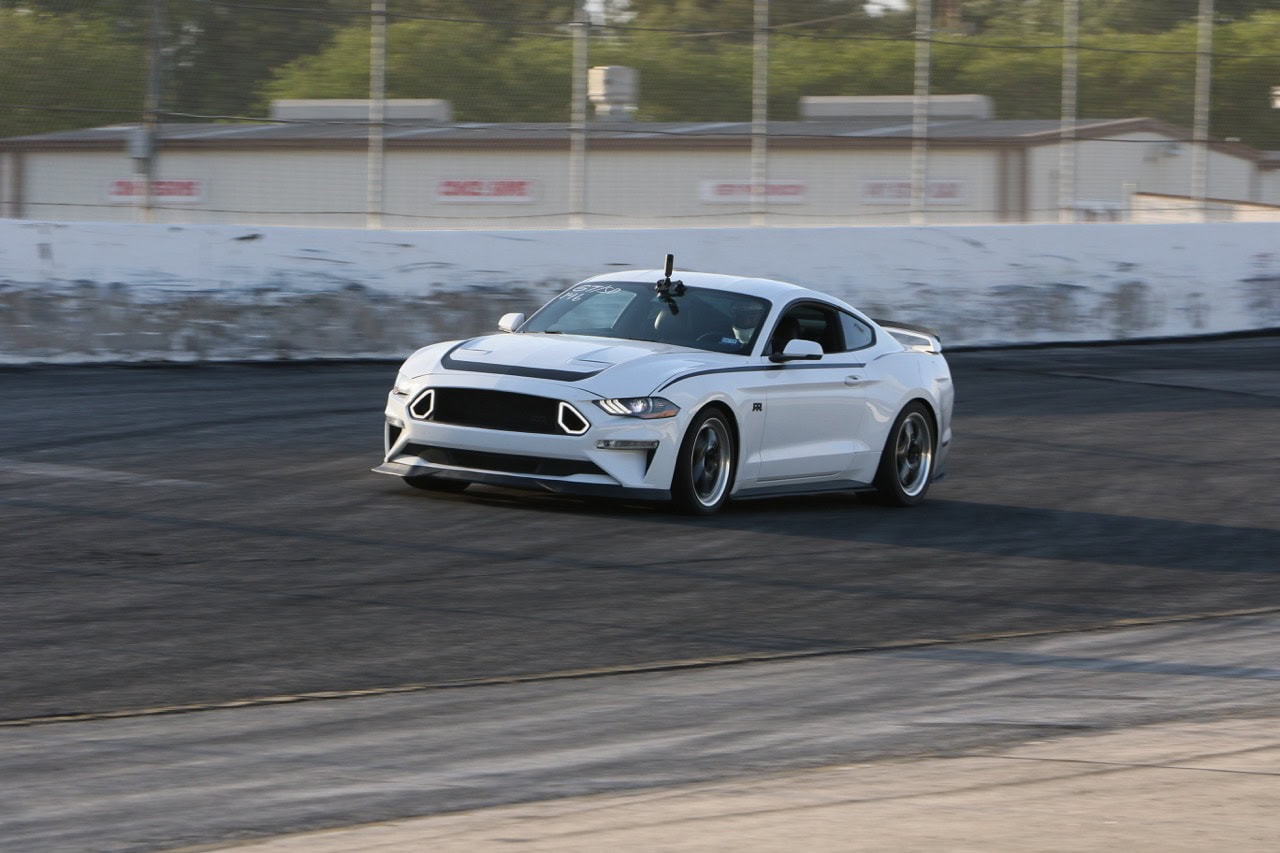 White Ford Mustang racing on track at Mustang Week event.