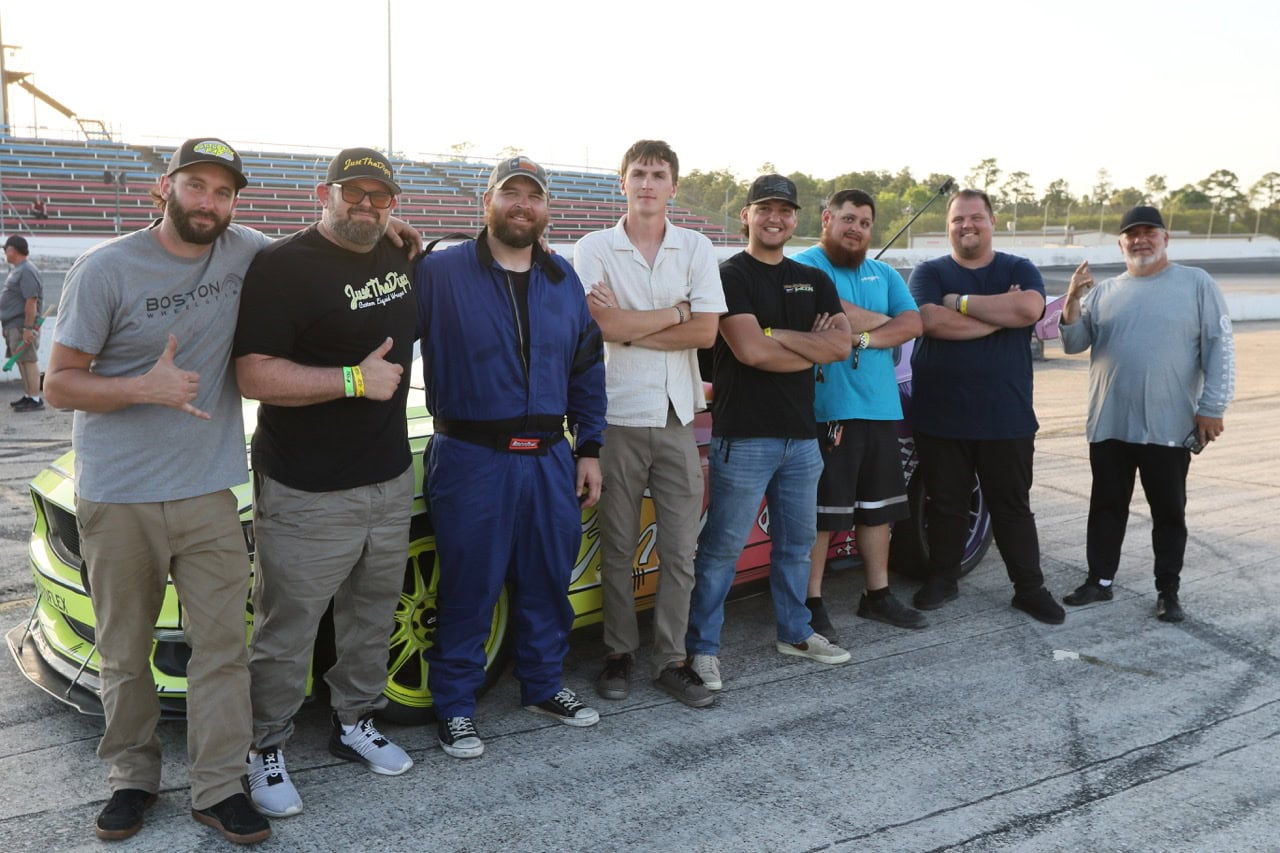 Group of car enthusiasts at Mustang Week event with customized Ford Mustangs.
