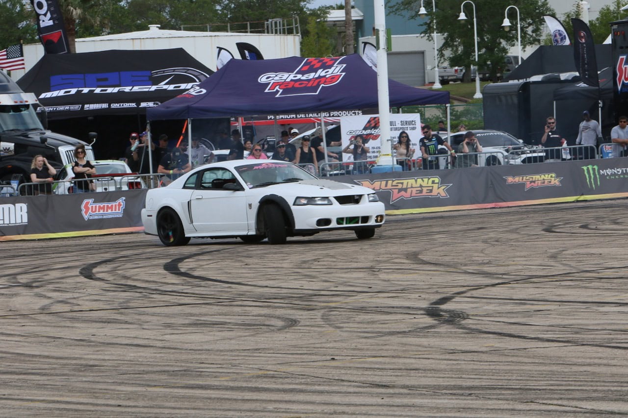 White Ford Mustang performing a drift at Mustang Week event.
