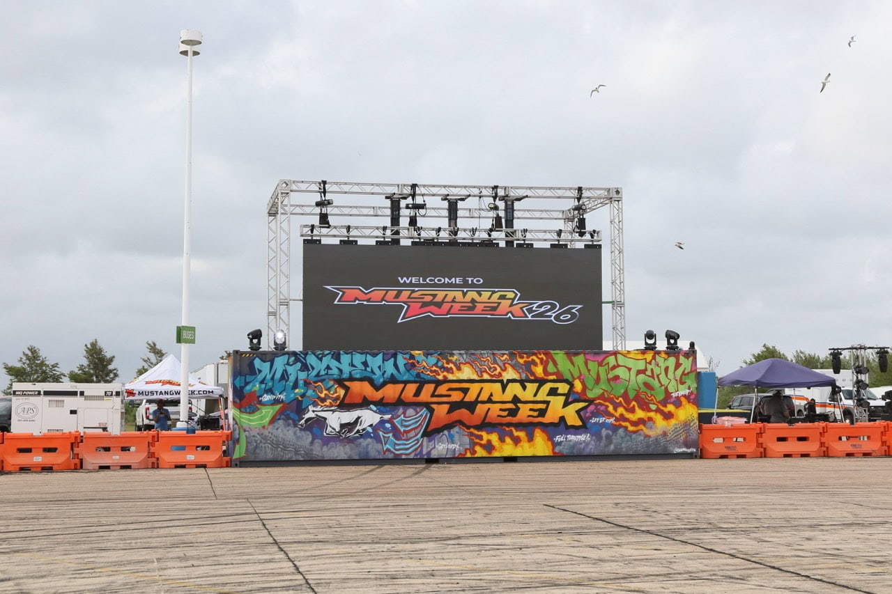 Mustang Week 2026 event stage with colorful banner and large screen.