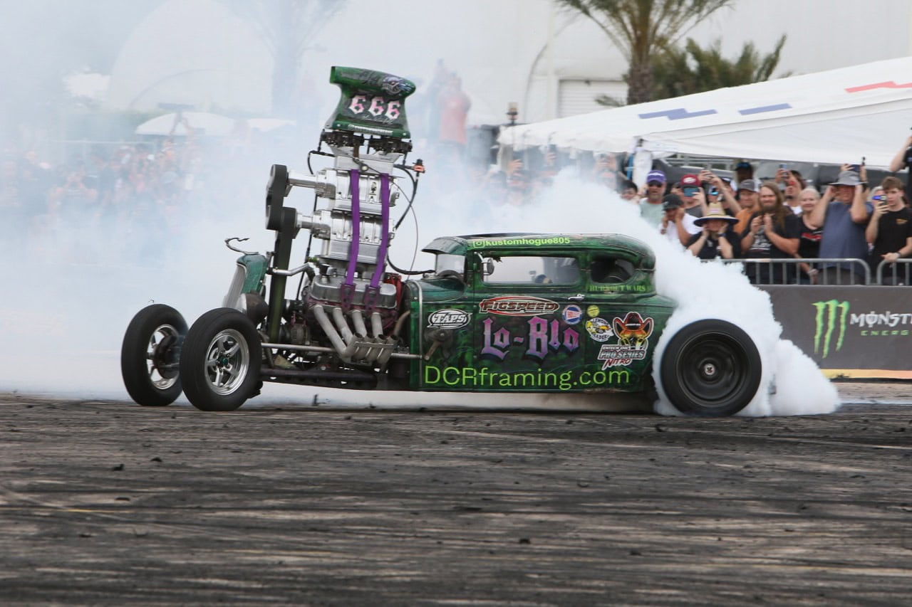 Custom drag racing car performing burnout at Mustang Week event.