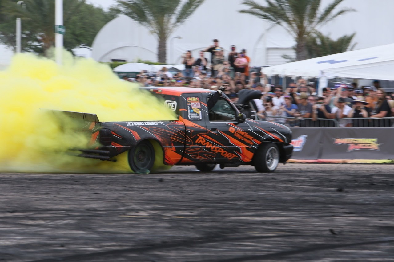 Custom black and orange Mustang drag car performing burnout at Mustang Week.