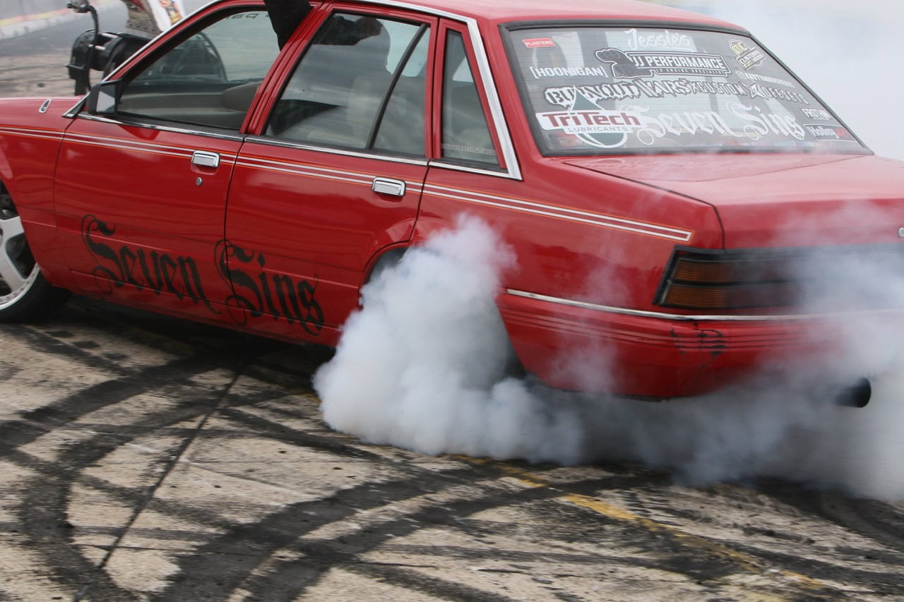 Red Mustang drag racing car performing burnout at Mustang Week event.