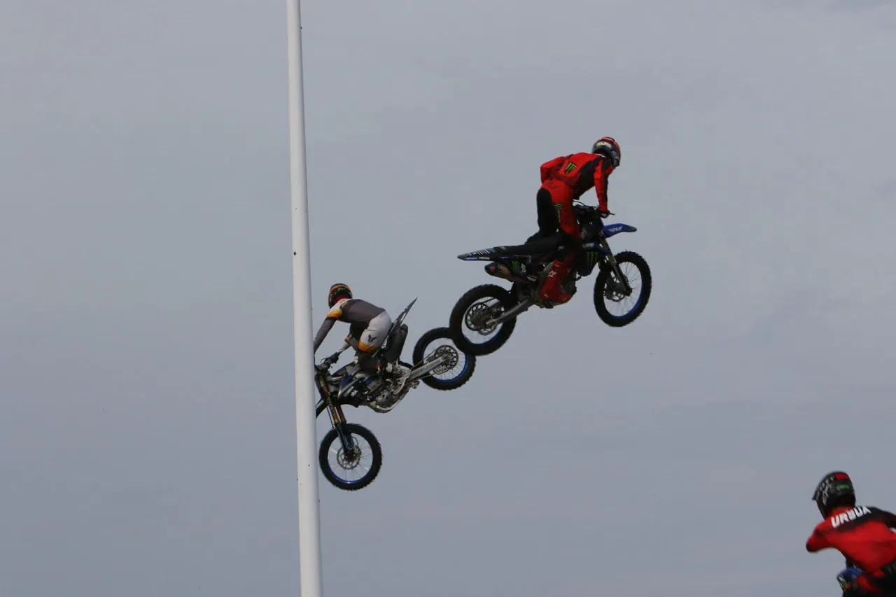 Two motocross riders in red and white gear jumping off a ramp during Mustang Week event.