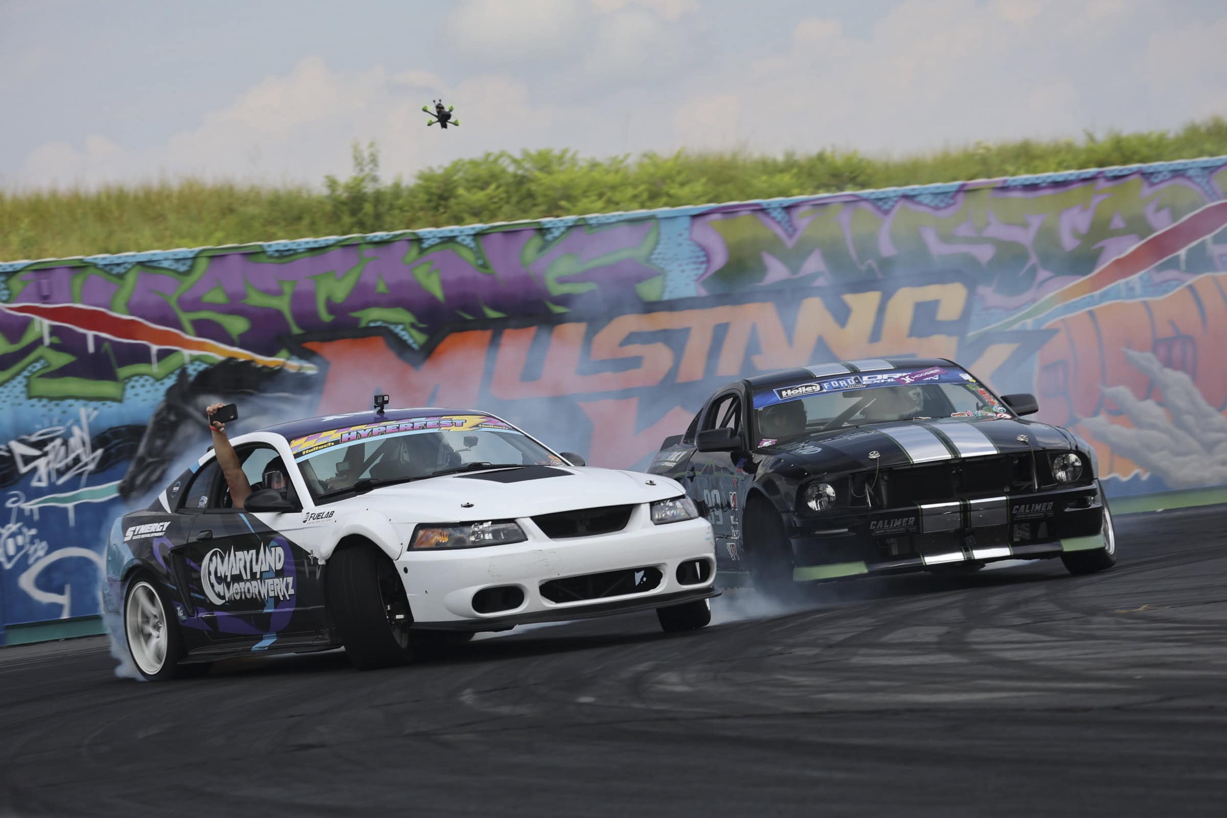 Two Ford Mustangs drifting on a race track during Mustang Week event.