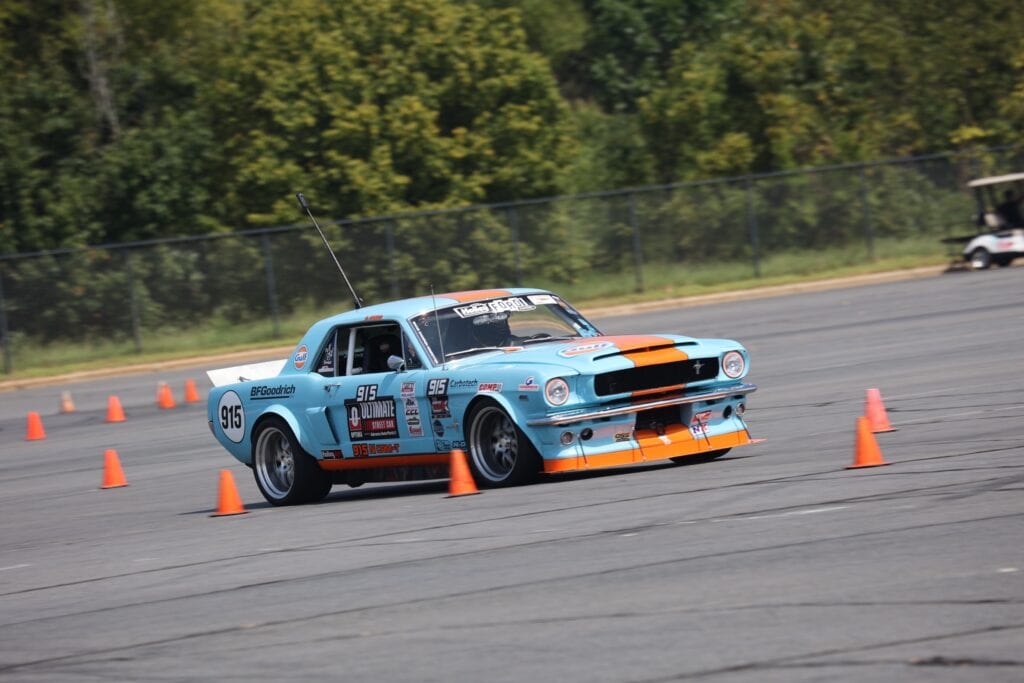 Blue vintage Mustang race car navigating through orange cones at Mustang Week Charlotte 2026.