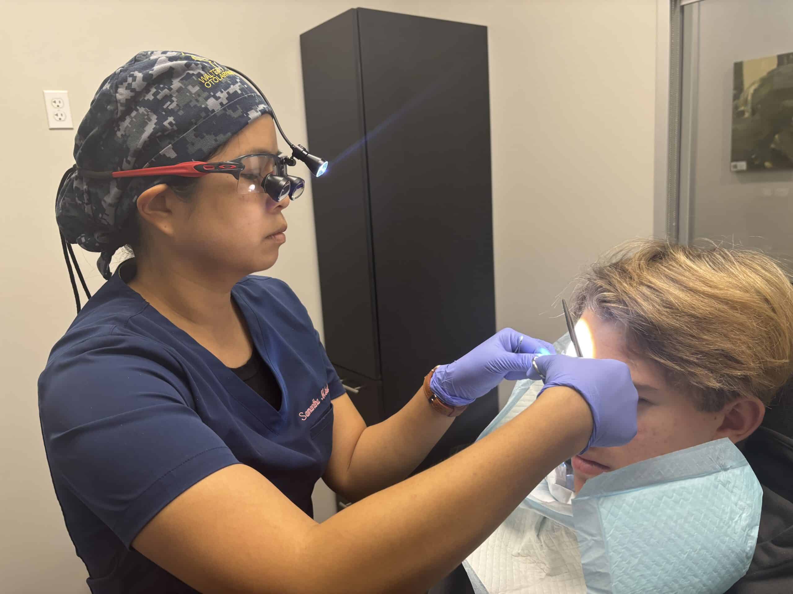 Dr. Samantha Mikals wearing a scrub cap and loupes performing a suturing procedure on the forehead of a patient.