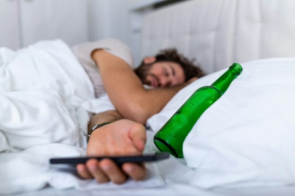 a man laying in bed sleeping with a beer bottle empty on a pillow