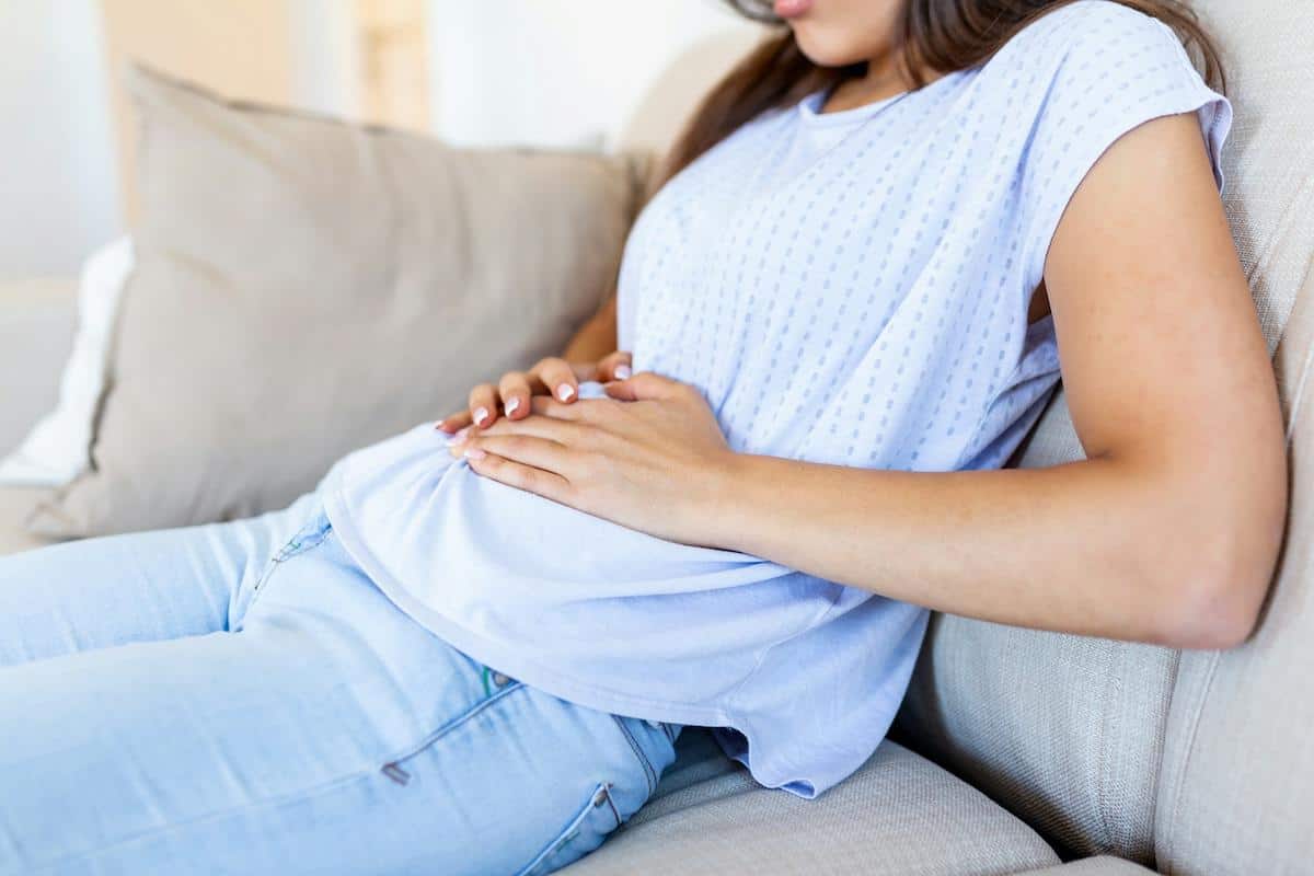 a lady holding her stomach in discomfort while sitting on the couch