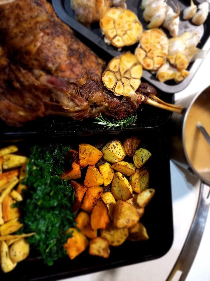 roast lamb shoulder, rasted garlic heads and a seperate tray of roasted vegetables. A saucepan with grave
