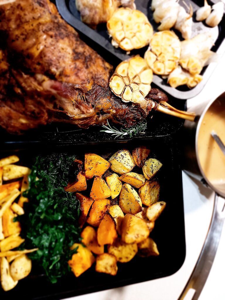 Lamb shoulder roast with roasted half garlic heads. An oven ray of roasted vegetables and a sauce pan with gravy