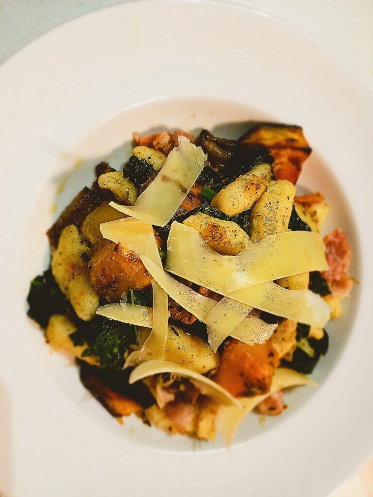 Roasted vegetable gnocchi in a white bowl plate parmesan cheese shavings on top