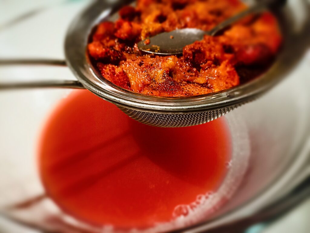 straining the strawberry tree pulp through a fine sieve. Collecting the liquid in a glass bowl underneath