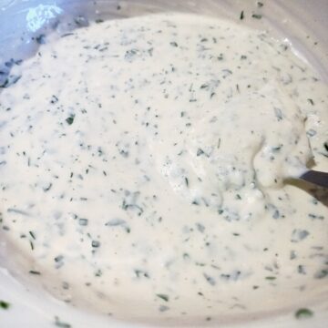 Mixing yoghurt mint dressing with a spoon in a white bowl.